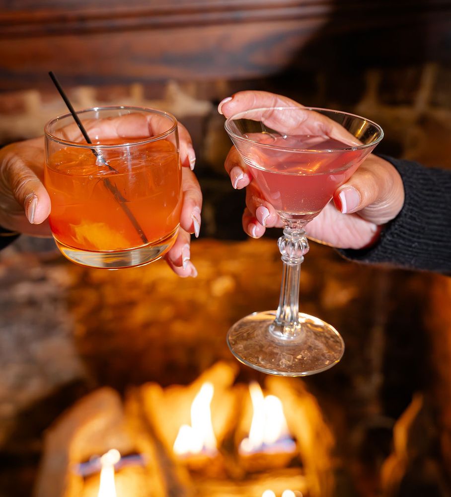 Two cocktails toasted before a crackling fireplace